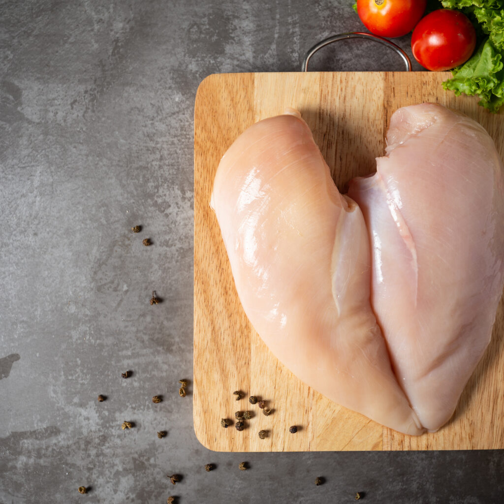Raw chicken breasts on wooden cutting board.